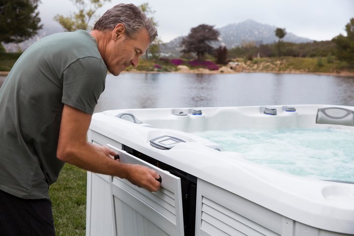 man opening sundance spa access panel to perform routine hot tub care