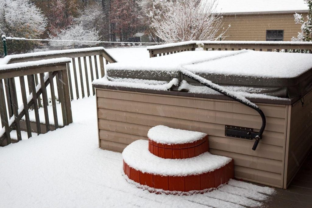 snow-covered hot tub cover on a backyard deck in winter
